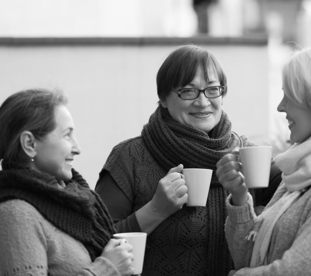 Mature women in warm clothes having cup of hot tea on terrace